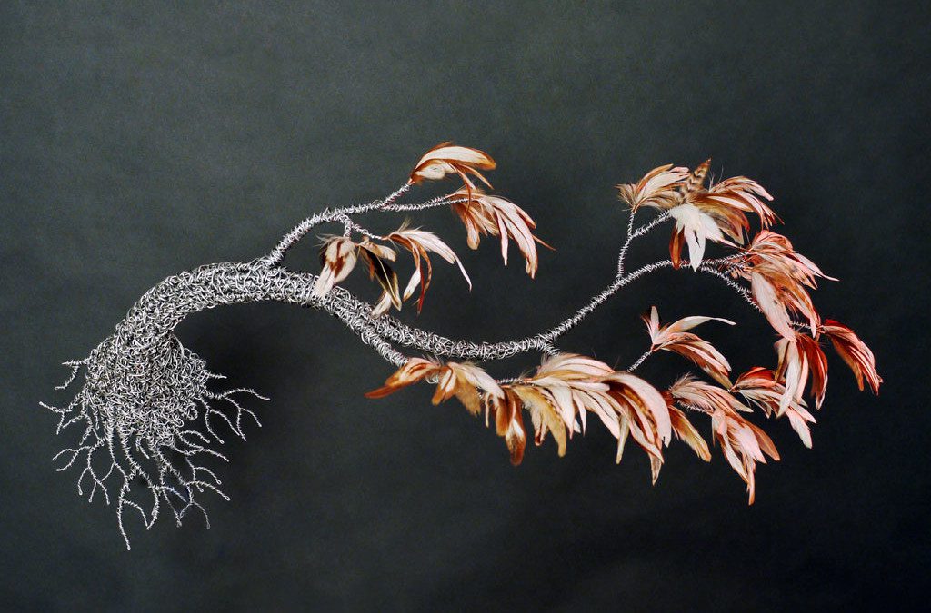 Woven metal tree with bird feathers as leaves.